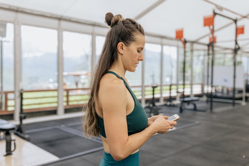 Female athlete in gym looking at phone, dressed in activewear for training.
